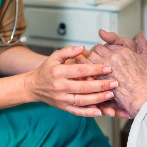 Female doctor giving encouragement to elderly patient by holding her hands